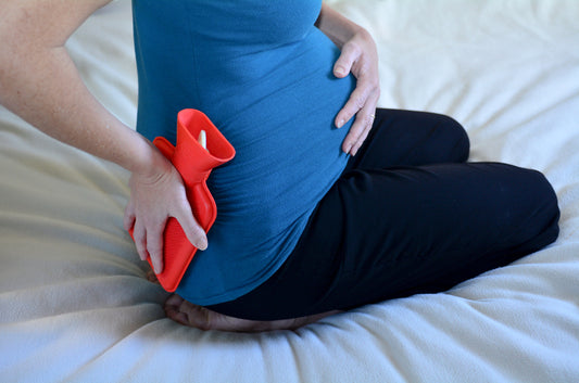 Image of pregnant woman holding a hot water bottle to her back to ease her pain